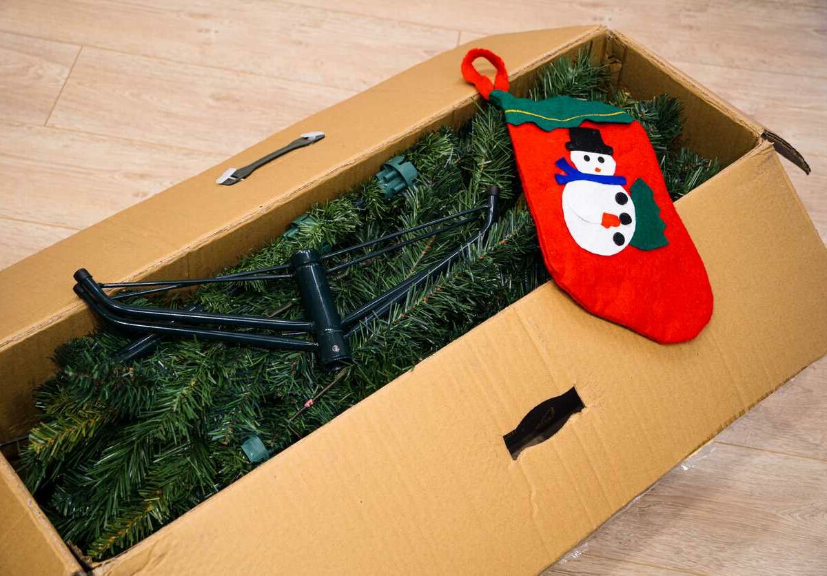 An artificial Christmas tree and snowman stocking folded in a cardboard box.