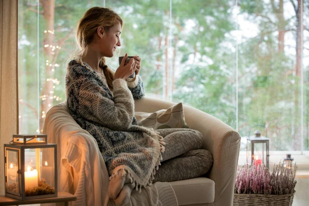Young woman enjoying a hot drink in a chair next to a large window.