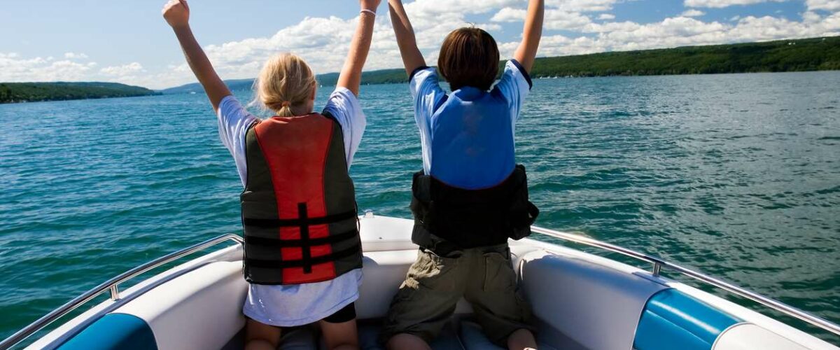 Two kids are at the front of a boat, wearing lifejackets.