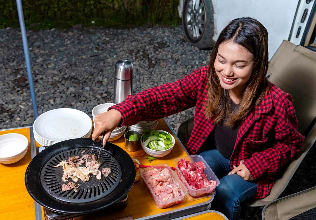 Young woman grilling meat outside of RV.