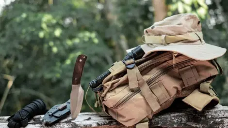 A hunting knife and bag sit on a log during hunting season.