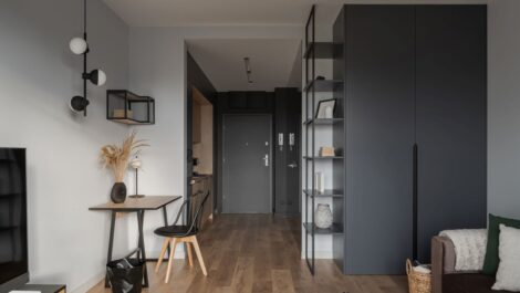 A stylish but small gray and white apartment with a couch, TV, writing desk, and galley kitchen.