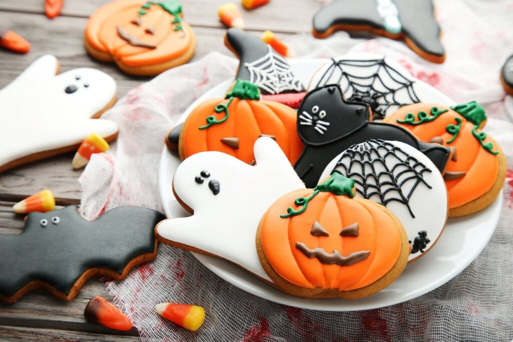 A plate of Halloween sugar cookies resembling jack-o’-lanterns, bats, ghosts, black cats, and other spooky items.