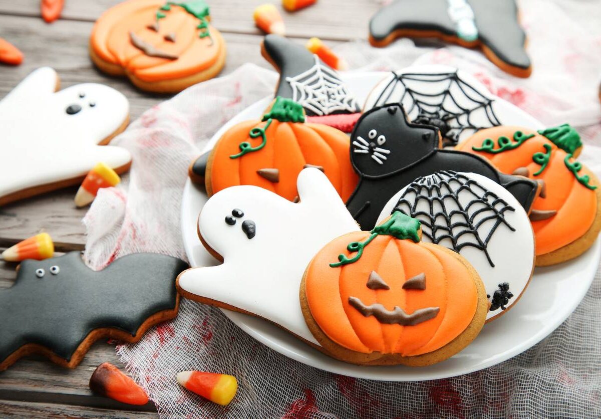 A plate of Halloween sugar cookies resembling jack-o’-lanterns, bats, ghosts, black cats, and other spooky items.