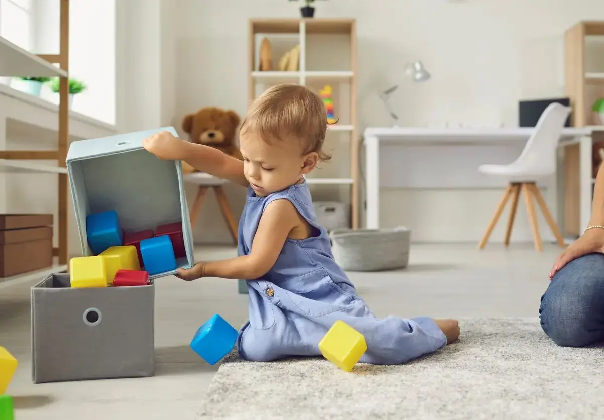 A toddler puts blocks back into their toy storage box