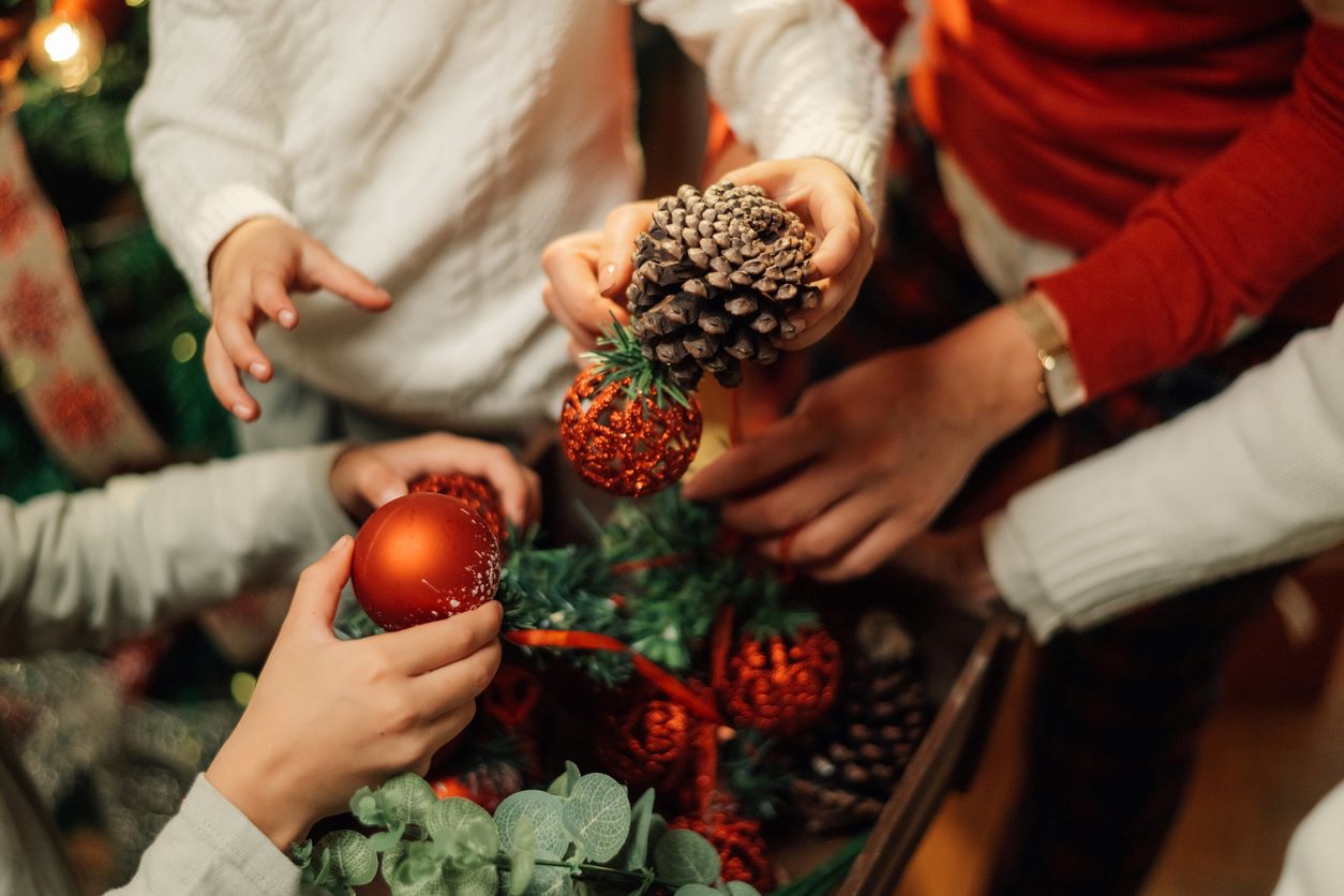 Hands packing red ornaments and pinecones into a box, preparing fragile Christmas decorations for seasonal storage.