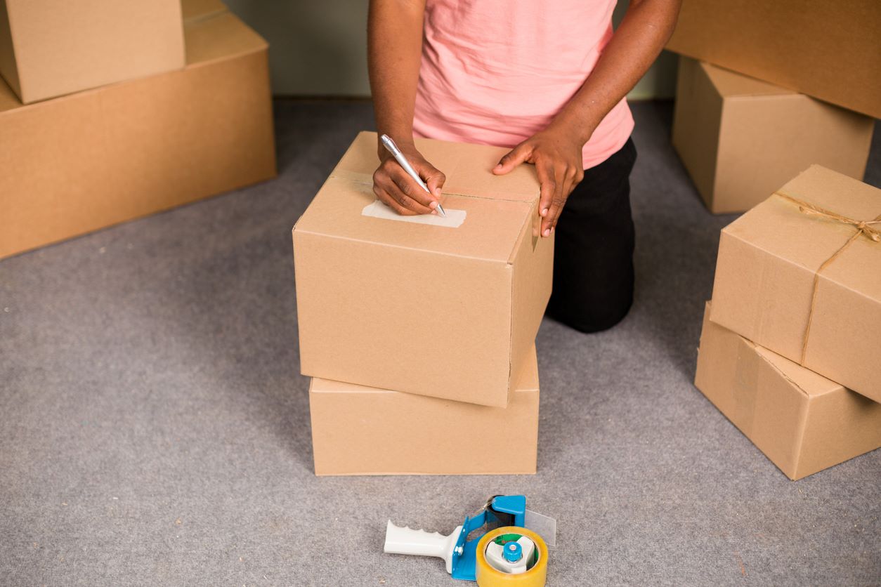 A person labeling cardboard boxes with a marker, organizing packed items for seasonal storage and easy access.
